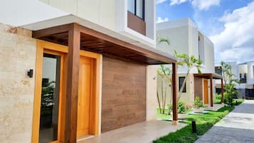 A modern residential building with a wooden entrance, tiled pathway, and a well-maintained garden.