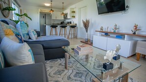 Een moderne woonkamer met een bank, een glazen salontafel en een aan de muur bevestigde televisie.