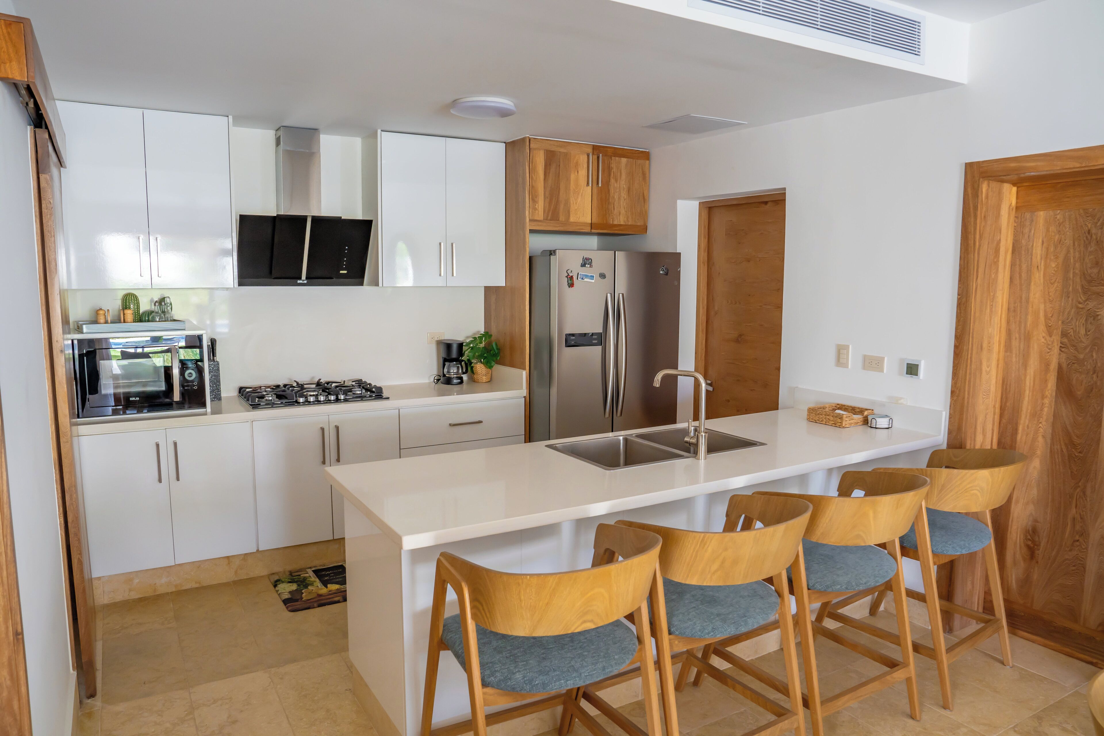 A modern kitchen with white cabinets, a stainless steel refrigerator, a gas stove, and a wooden island with bar stools.