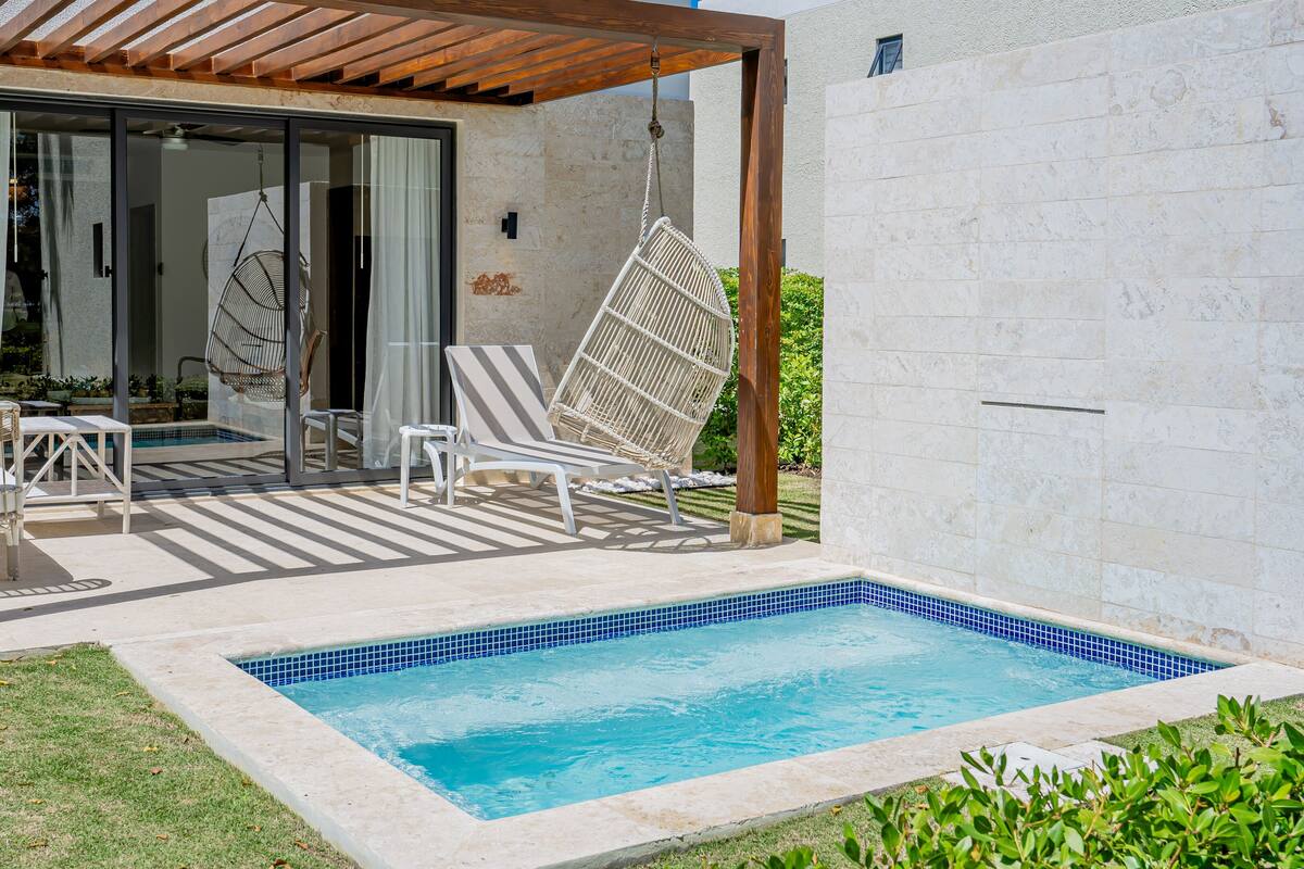 Un espace piscine comprenant une petite piscine, des chaises longues et une pergola.