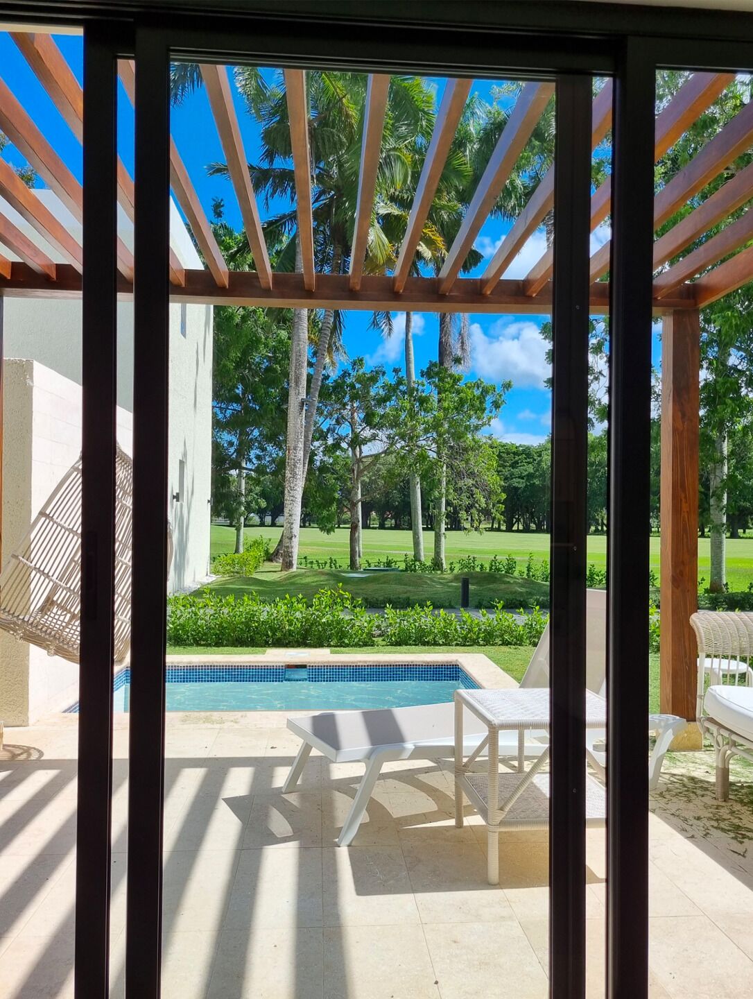 Un espace extérieur abrité comprenant une piscine, des chaises longues et une vue sur un terrain de golf.