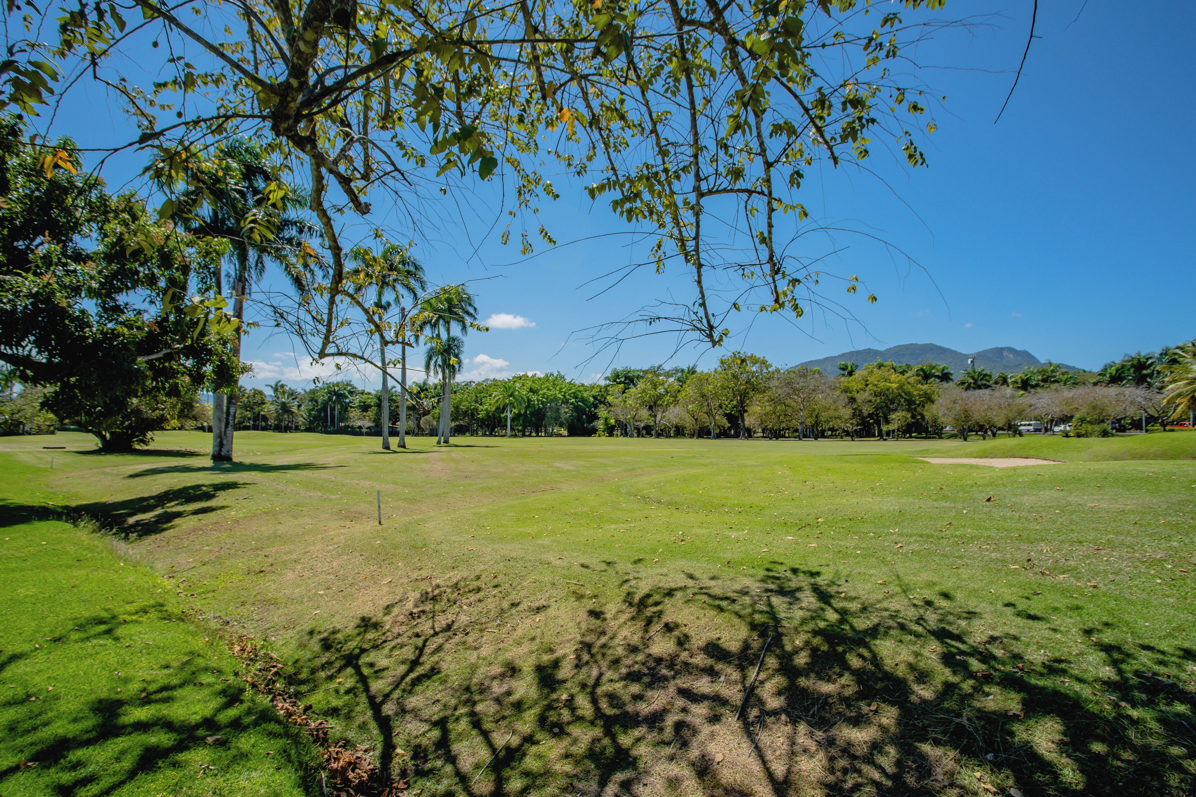Un parcours de golf avec un ciel dégagé, des arbres et des montagnes à l’horizon.