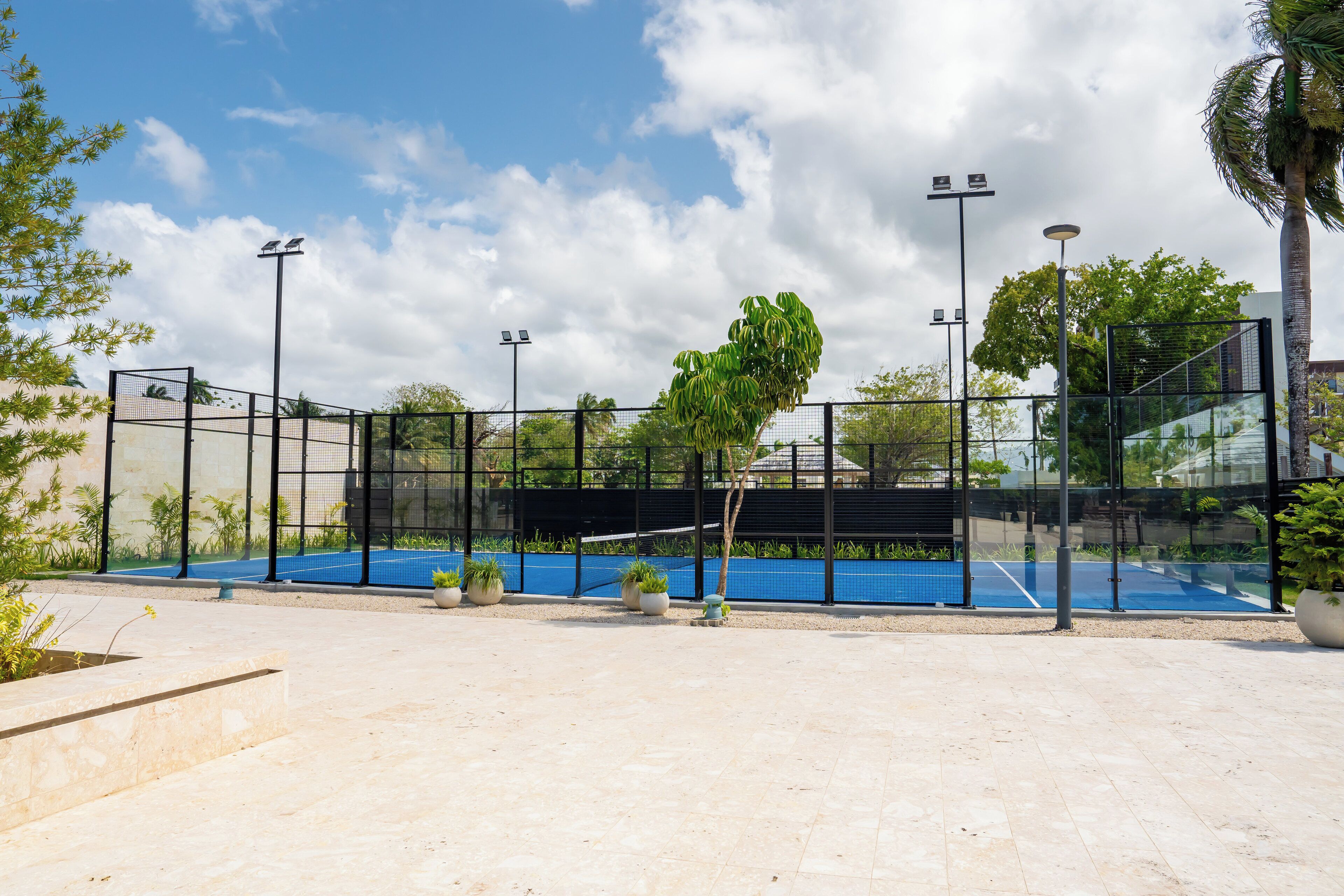 An outdoor tennis court with a net, surrounded by a fence, and potted plants.