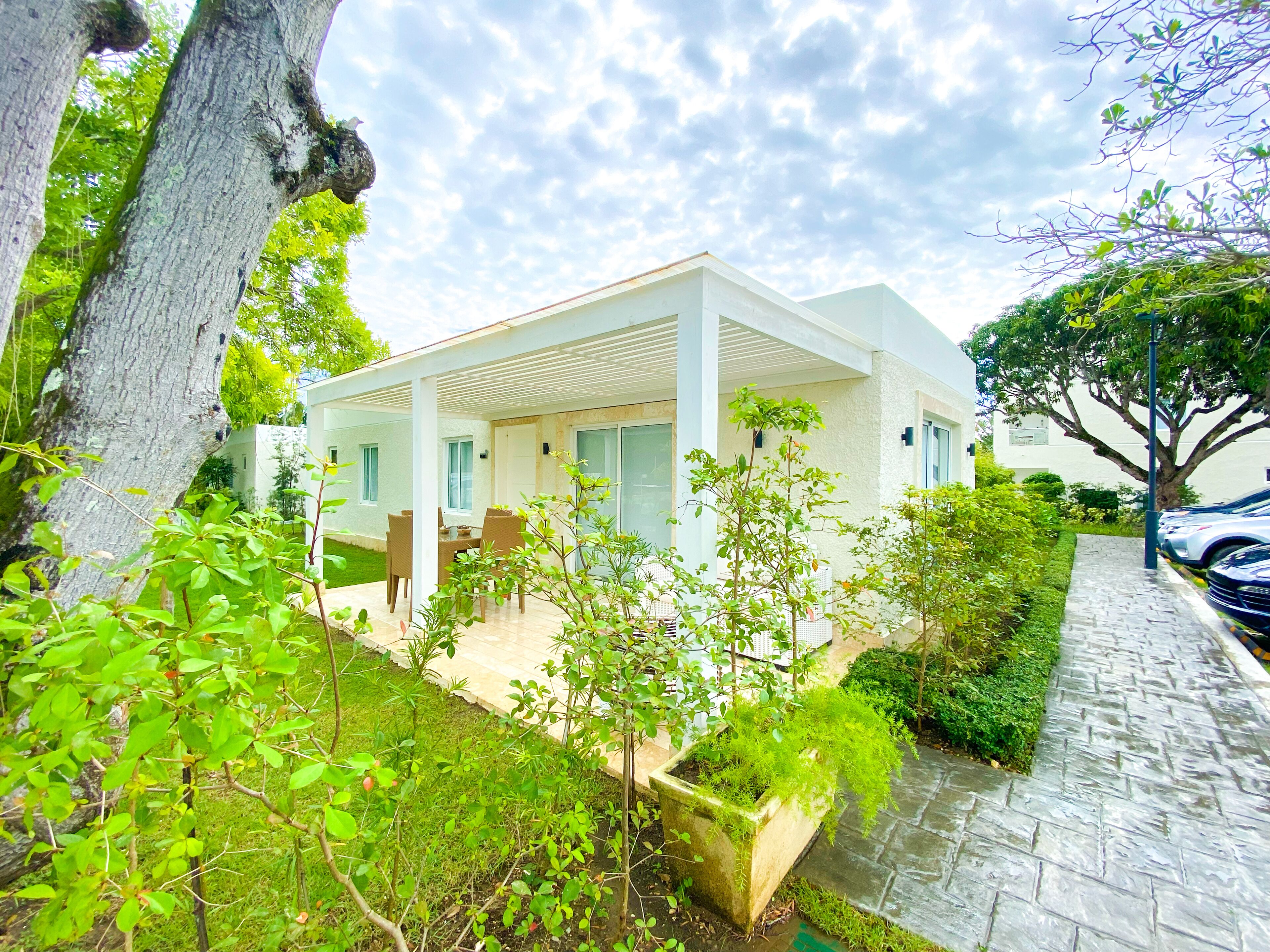 A modern house with a patio, surrounded by greenery and a paved walkway.
