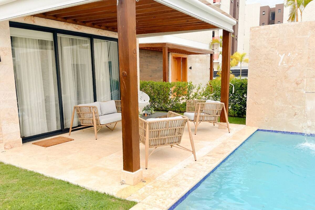 Un espace extérieur abrité doté d'une piscine, de meubles en osier et d'une porte vitrée donnant sur une pièce.