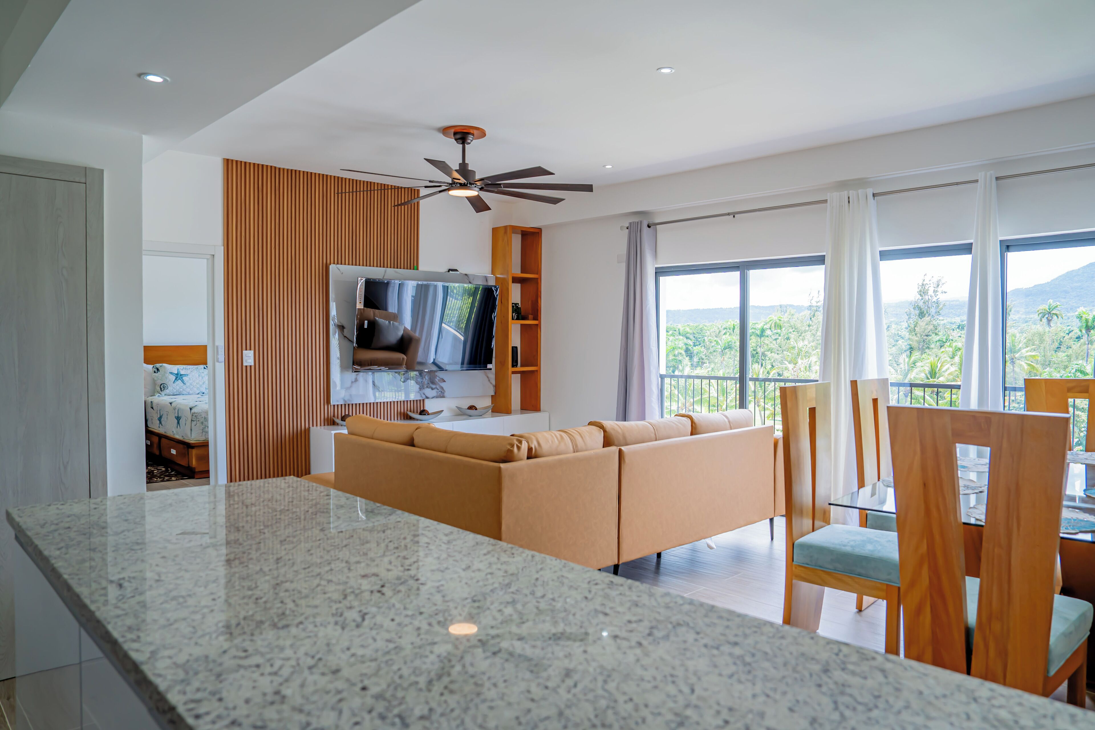 Una sala de estar moderna con un televisor grande, un sofá y un comedor con sillas de madera y una mesa de vidrio.