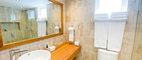 A modern bathroom with a large mirror, a round sink, a toilet, and a shower area.