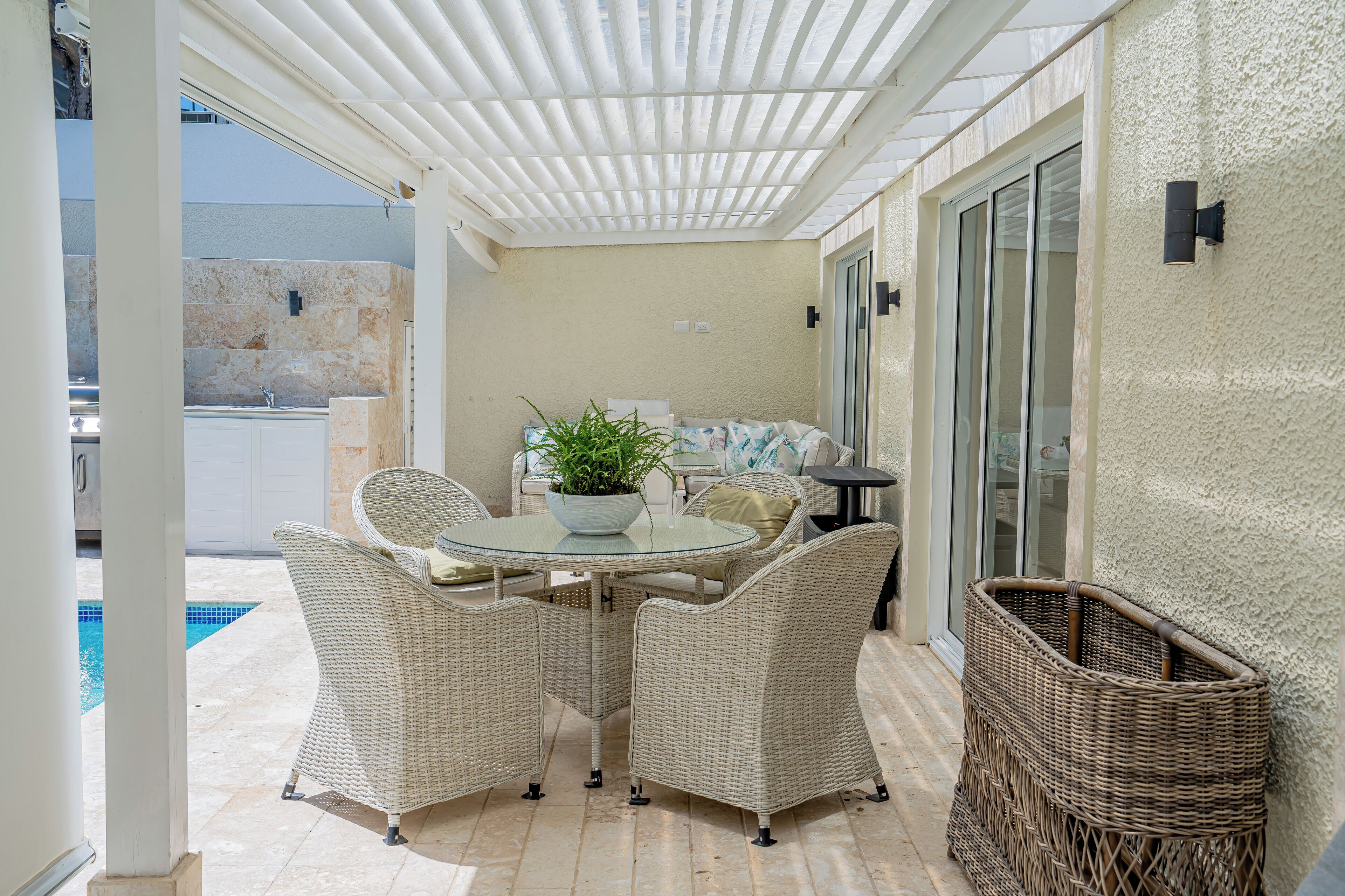 A covered patio area with wicker furniture, a glass table, and a potted plant.