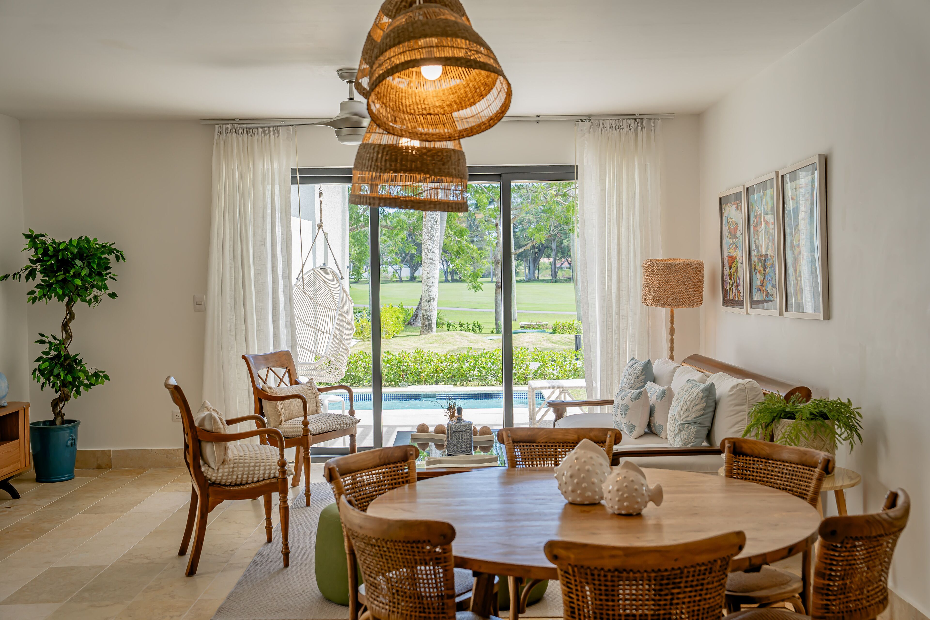 A dining area with a round wooden table, wicker chairs, and a hanging wicker light fixture.