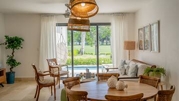 A dining area with a round wooden table, wicker chairs, and a hanging wicker light fixture.
