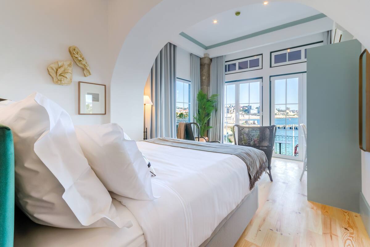 A modern hotel room with a large bed, a view of the city, and a balcony with a view of the sea.