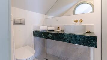 A modern bathroom with a white toilet, a marble vanity with a sink, and a mirror above the vanity.