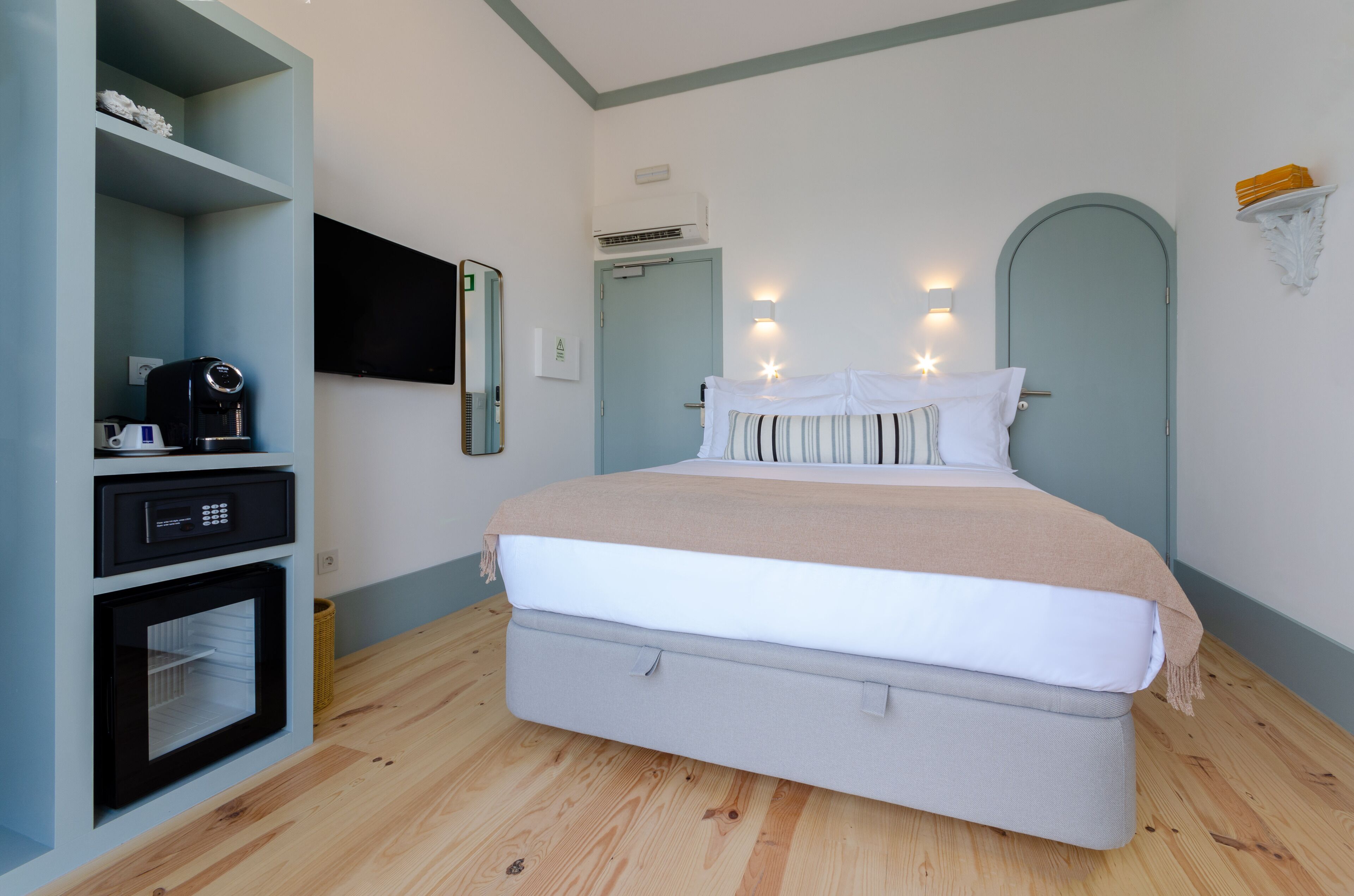A bedroom with a bed, a built-in coffee maker, a television, and a wall-mounted shelf.