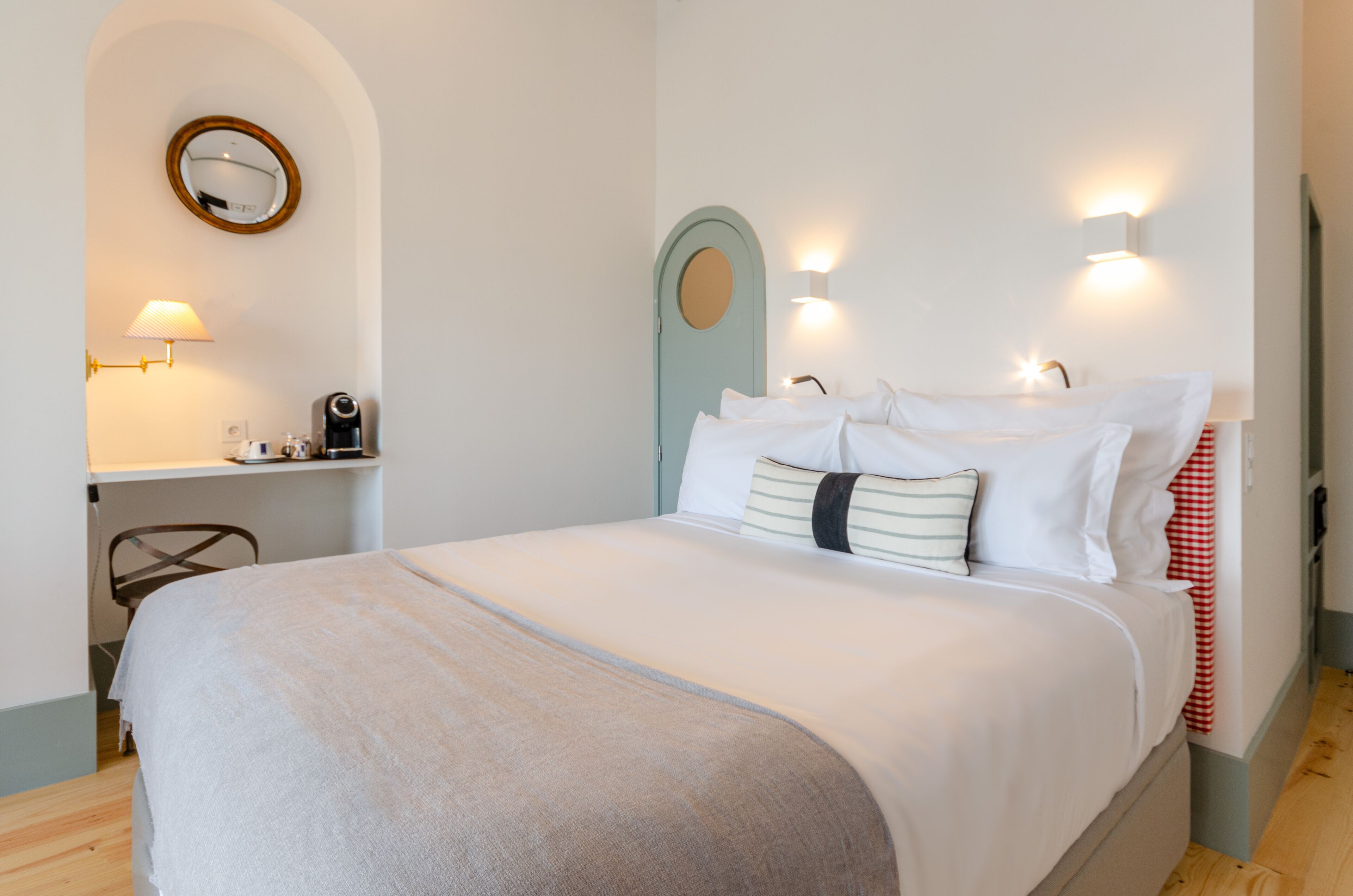 Une chambre à coucher bien rangée, avec un lit, une table de chevet, une lampe et un miroir au mur.
