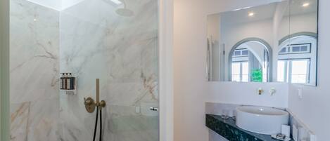 A modern bathroom with a marble shower, a sink with a large mirror, and a curved countertop.