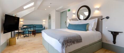 Una habitación de hotel moderna con una cama grande, un televisor de pantalla plana, una zona de comedor con mesa y sillas, y un techo con tragaluces.