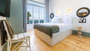 A bedroom with a large bed, a chair, a TV, and a view of the sea. - Westlight Cascais Chalet - Adults Only. (Cascais)