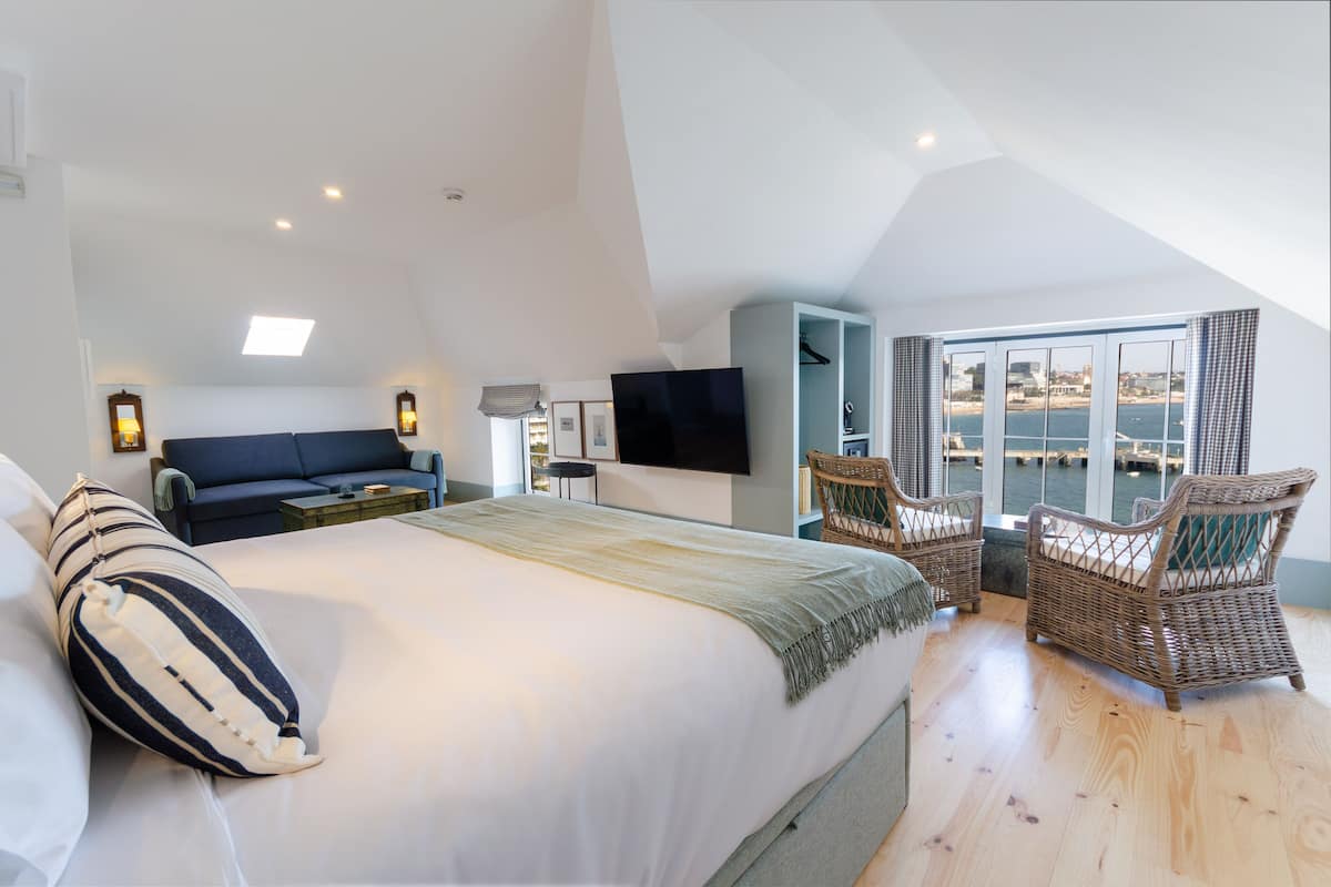 A bedroom with a large bed, a sofa, a TV, wicker chairs, and a view of the sea.