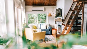 A cozy living room with a sofa, a chair, a fireplace, and a wooden ladder. - THE NEST ~ Charming  cabin escape ~ Hot tub ~ Suana ~ Bbq (Lenhartsville)