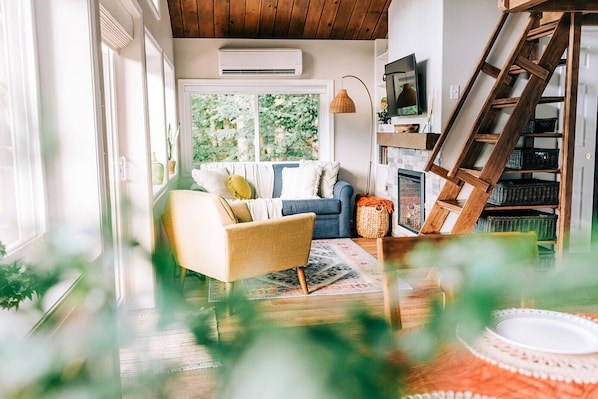 A cozy living room with a sofa, a chair, a fireplace, and a wooden ladder. - THE NEST ~ Charming  cabin escape ~ Hot tub ~ Suana ~ Bbq (Lenhartsville)