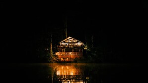 A two-story wooden cabin with a balcony, surrounded by trees and reflecting on the water. - THE NEST ~ Charming  cabin escape ~ Hot tub ~ Suana ~ Bbq (Lenhartsville)