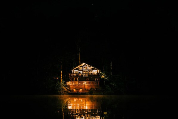 A two-story wooden cabin with a balcony, surrounded by trees and reflecting on the water. - THE NEST ~ Charming  cabin escape ~ Hot tub ~ Suana ~ Bbq (Lenhartsville)
