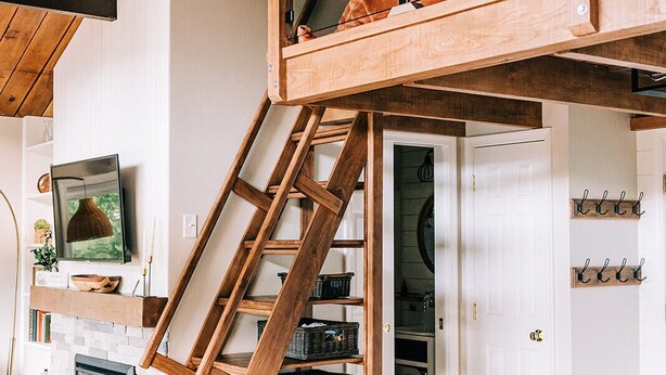 A loft-style room with a wooden ladder leading to a loft bed, a fireplace, and a white door with hooks. - THE NEST ~ Charming  cabin escape ~ Hot tub ~ Suana ~ Bbq (Lenhartsville)