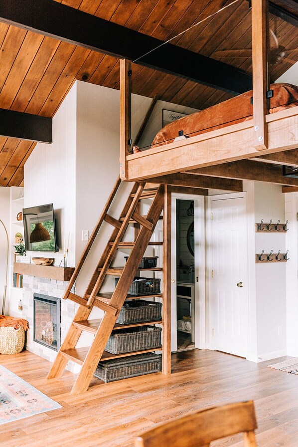 A loft-style room with a wooden ladder leading to a loft bed, a fireplace, and a white door with hooks. - THE NEST ~ Charming  cabin escape ~ Hot tub ~ Suana ~ Bbq (Lenhartsville)