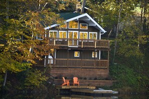 A multi-story wooden cabin with a balcony, surrounded by trees.