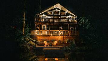 A two-story wooden cabin with a balcony, a deck, and a small outdoor seating area.