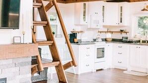 A kitchen with white cabinets, a wooden staircase, and a loft bed. - THE NEST ~ Charming  cabin escape ~ Hot tub ~ Suana ~ Bbq (Lenhartsville)