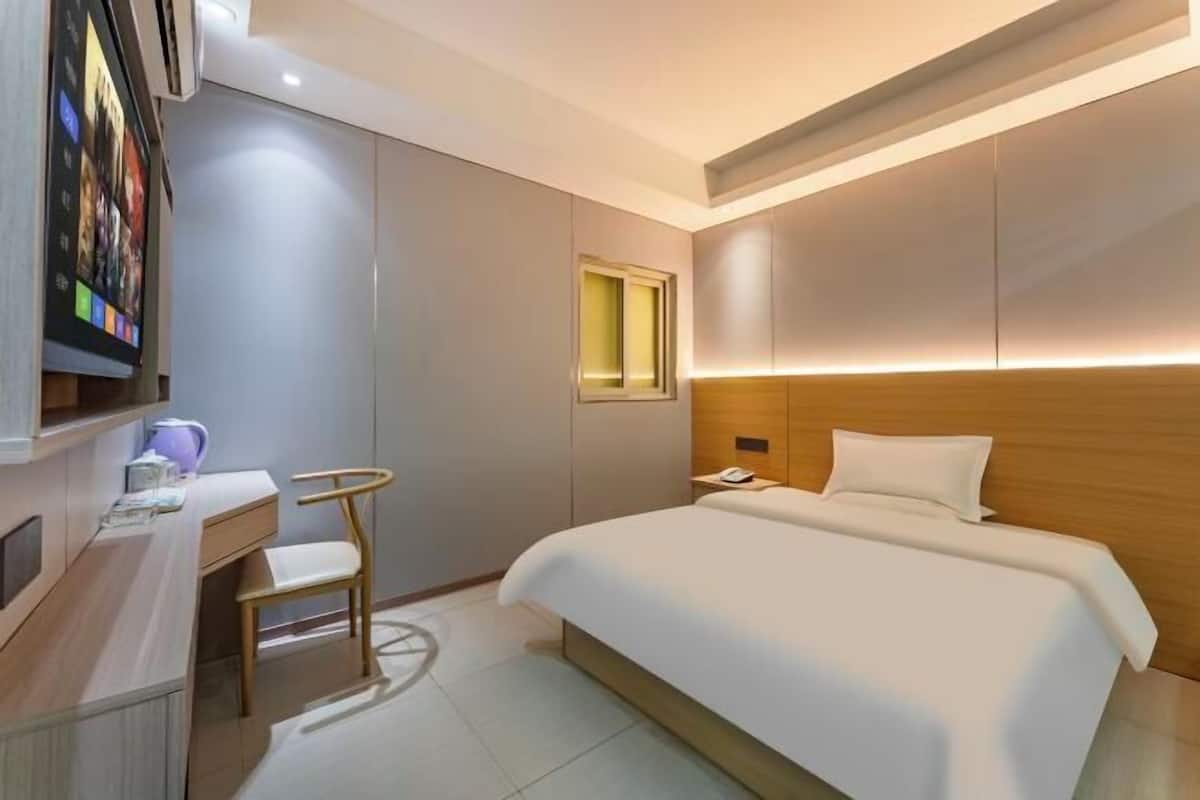 A hotel room with a bed, bedside table, chair, desk, TV, and a window.