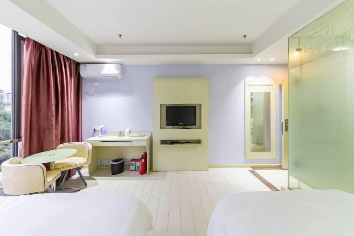 A hotel room with a bed, a desk with a chair, a television, and a window with curtains.