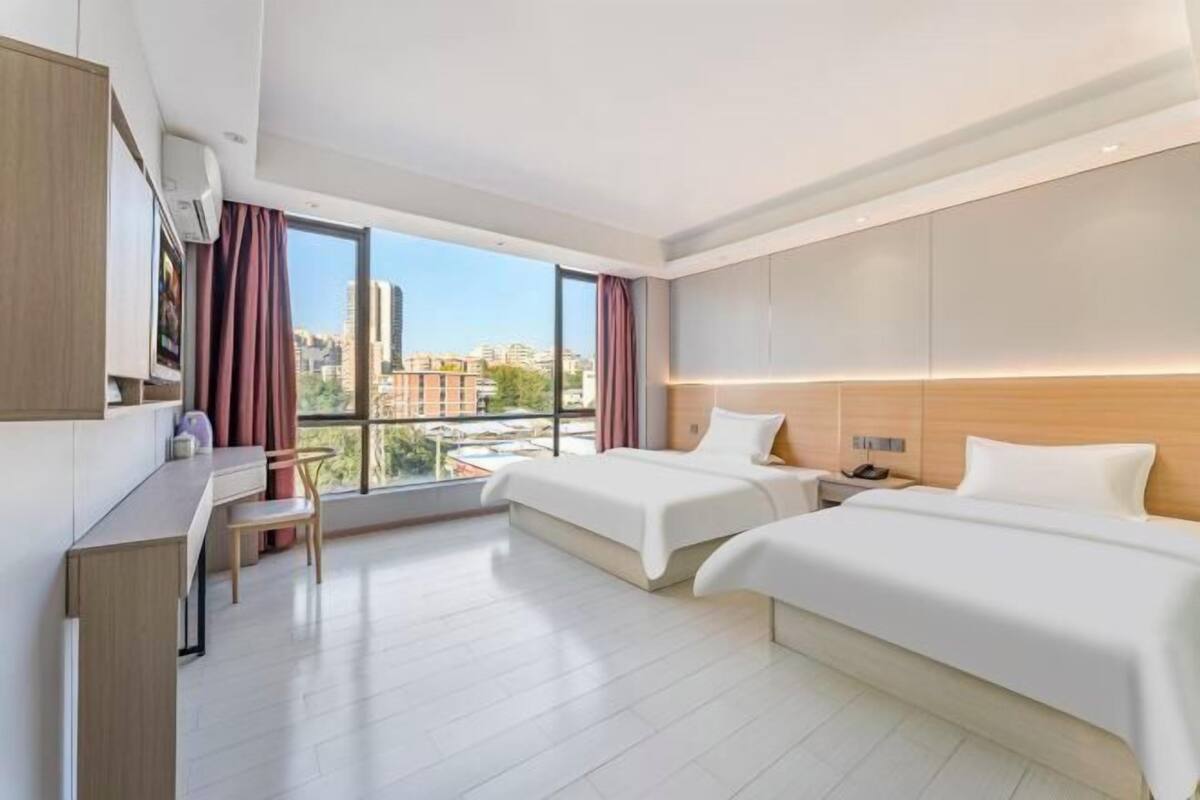 A modern hotel room with two beds, a desk, and a chair.