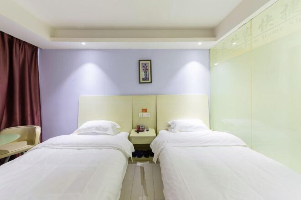 A hotel room with two single beds, a bedside table with a lamp, a mirror, and a wardrobe.