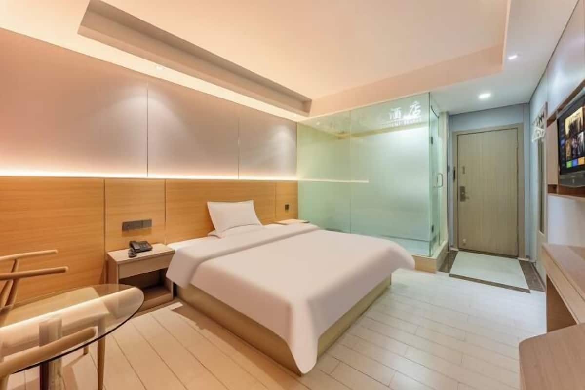 A modern hotel room with a large bed, bedside table, and a glass table.