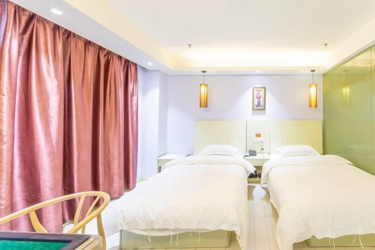 A hotel room with two single beds, a bedside table, a chair, and a large window with curtains.