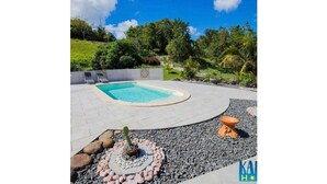 En swimmingpool med fliseterrasse, omgivet af en anlagt have med sten og en dekorativ plantekasse.