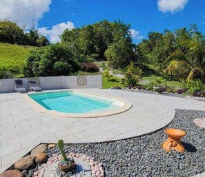 Una piscina con borde de baldosas, rodeada por un jardín ajardinado con rocas y una maceta decorativa.