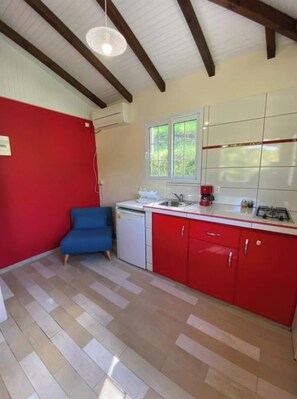 Una cocina funcional con armarios rojos, una silla azul y un lavavajillas pequeño.