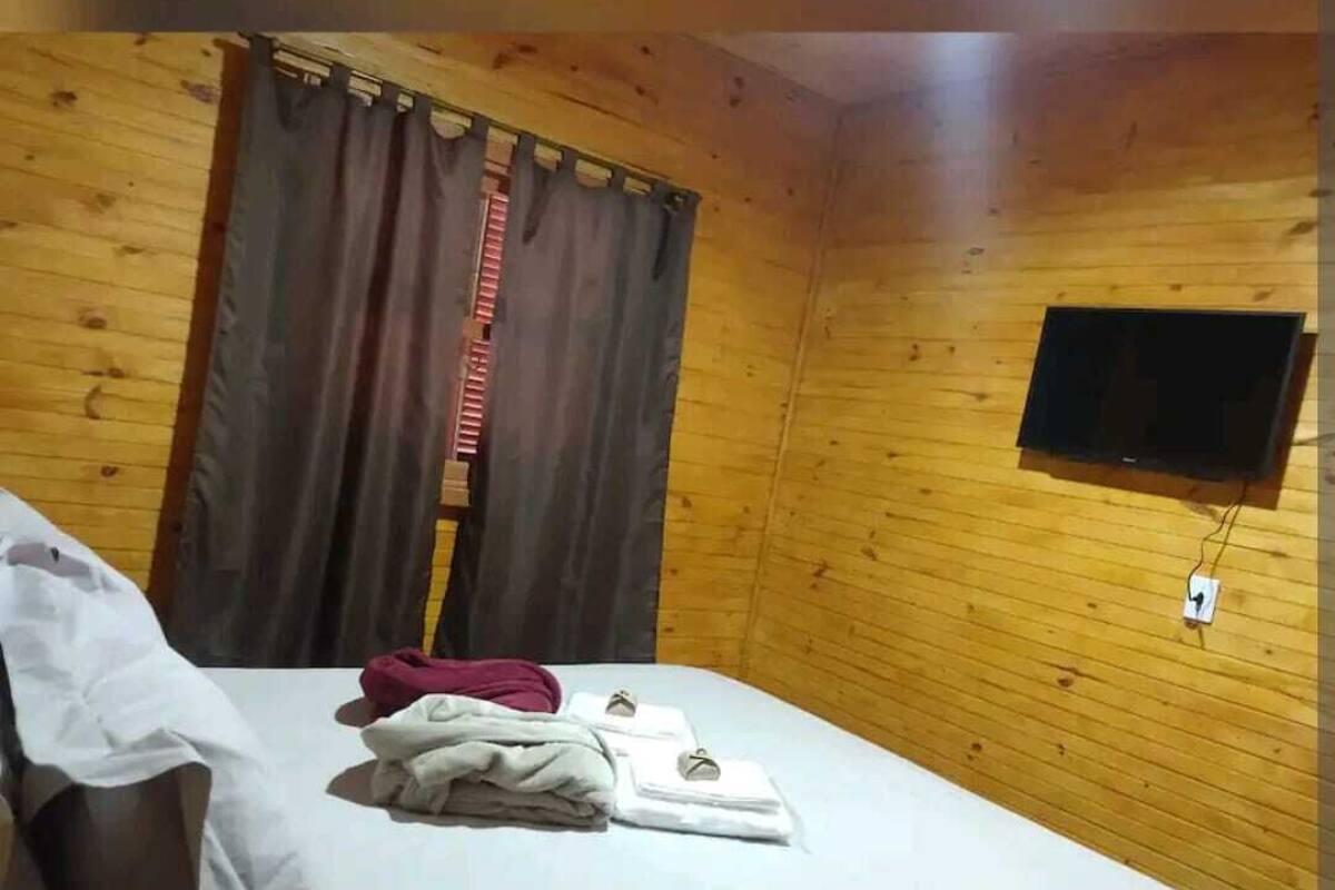 Une pièce aux murs lambrés, avec un lit, un téléviseur fixé au mur et une fenêtre avec des rideaux.