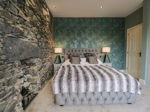 A bedroom with a stone wall, a tufted headboard, and a floral wallpaper.