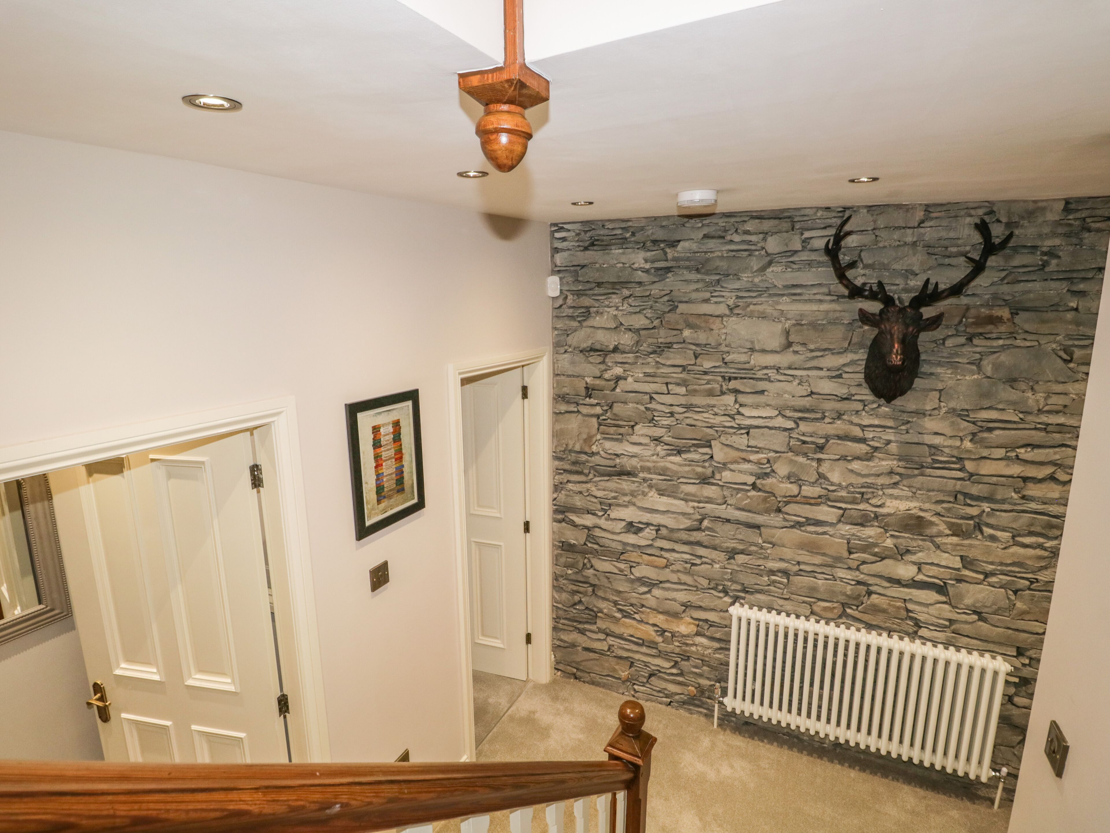 Un escalier avec une rampe en bois menant à un palier doté d’un mur en pierre et orné d’une tête de cerf fixée au mur.