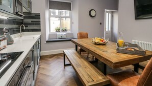 A modern kitchen with a wooden dining table, bench seating, and a breakfast setting with fruit and juice. - The Haven (Windermere)