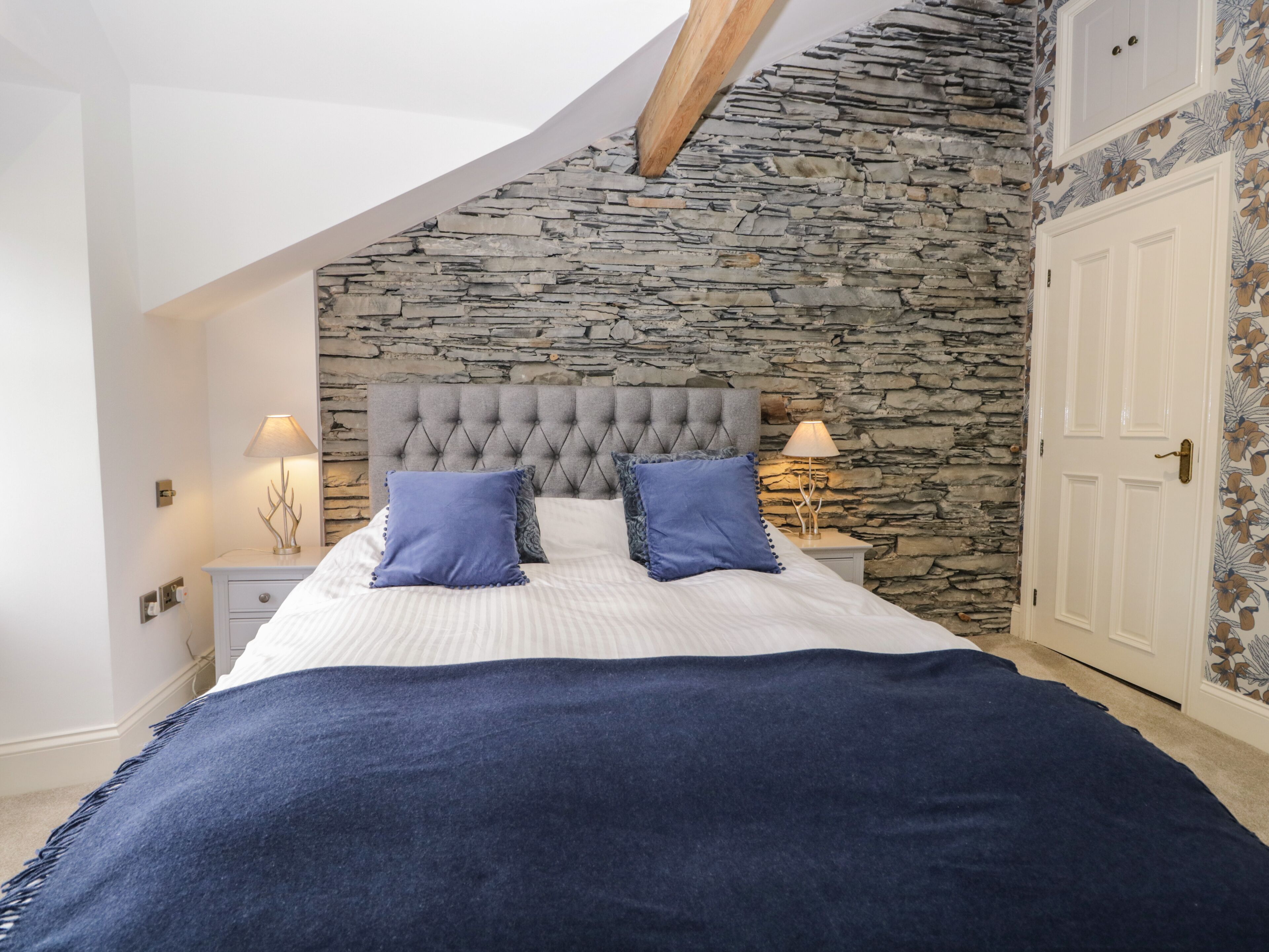 A bedroom with a stone wall, a tufted headboard, and a bed with blue pillows.