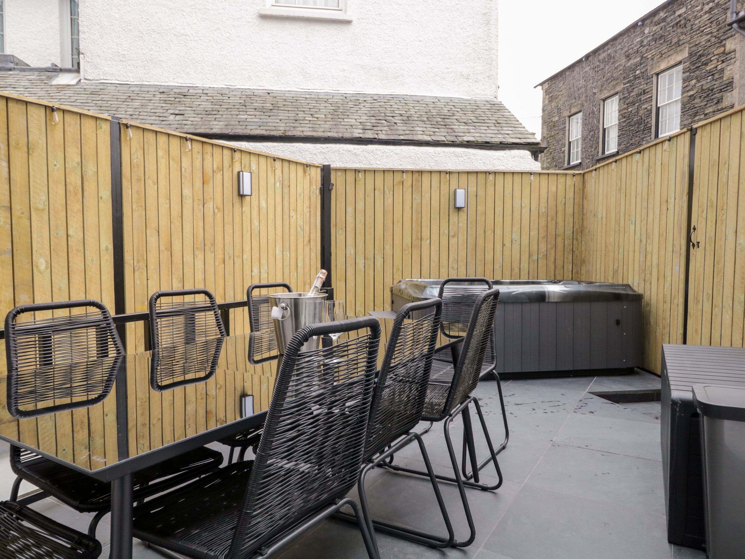 Een terras buiten met een tafel, stoelen, een jacuzzi en een houten omheining.