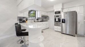 A modern kitchen with white cabinetry, stainless steel appliances, and a central island with bar stools. - Brand New Renovated COZY Home! Prime Location! Live in Style 🏡🌟⭐️💫 (Miami)