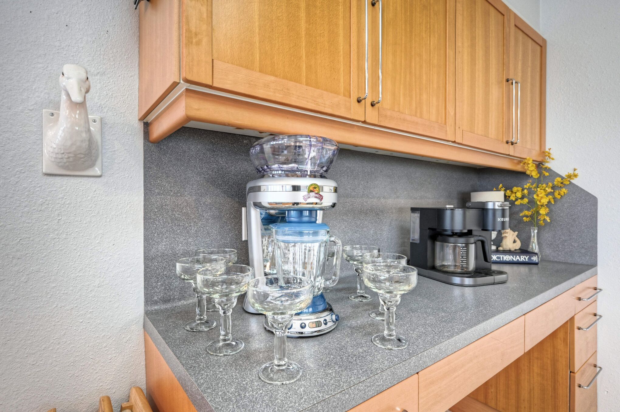 Et køkken med kaffemaskine, blender og flere glas på bordet.
