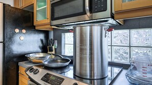 Une cuisine équipée d’une cuisinière en acier inoxydable, d’un four à micro-ondes et d’une grande casserole sur laquelle est inscrit : « ATTENTION – CHAUD ».