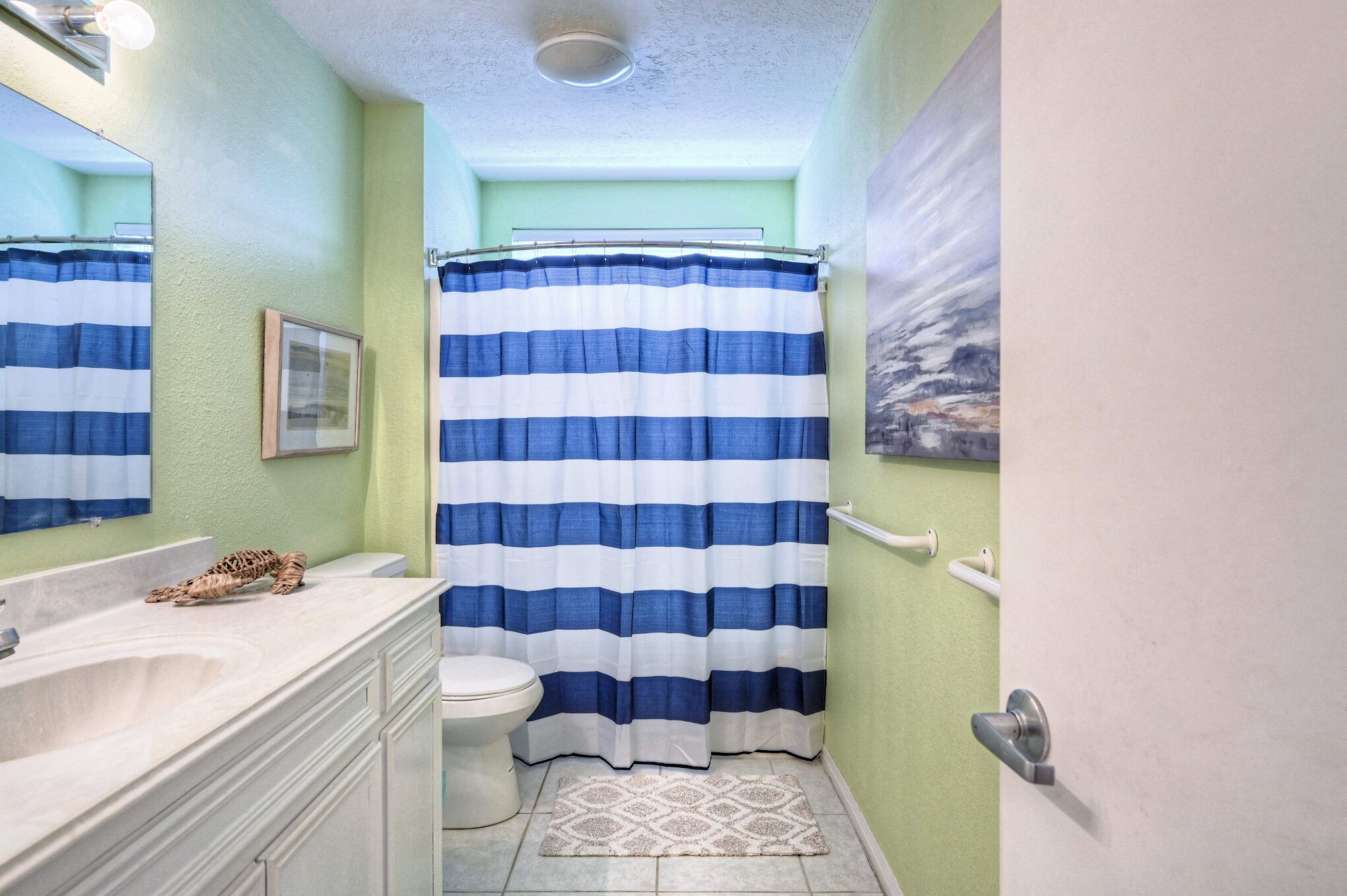 A bathroom with a striped shower curtain, a toilet, a sink, and a mirror.